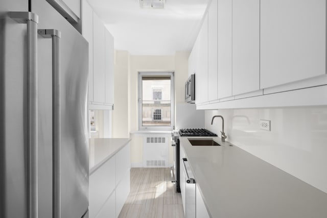 kitchen with white cabinetry, appliances with stainless steel finishes, sink, and radiator heating unit