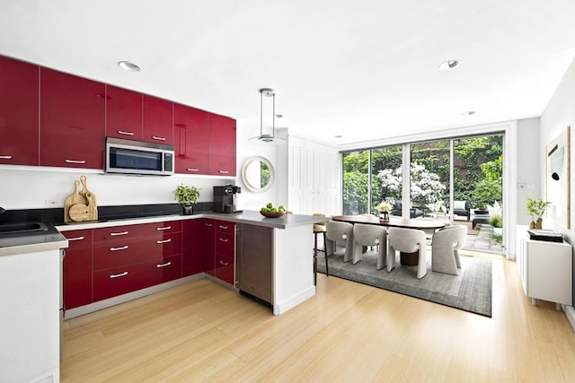kitchen featuring red cabinetry, a peninsula, stainless steel microwave, expansive windows, and light wood finished floors