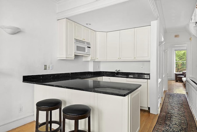kitchen with crown molding, a breakfast bar area, white microwave, light wood-type flooring, and white cabinets