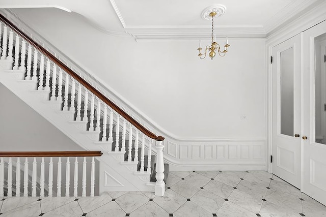 foyer entrance with stairs, crown molding, an inviting chandelier, and a wainscoted wall