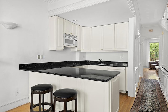 kitchen with crown molding, a kitchen breakfast bar, light hardwood / wood-style floors, and white cabinets