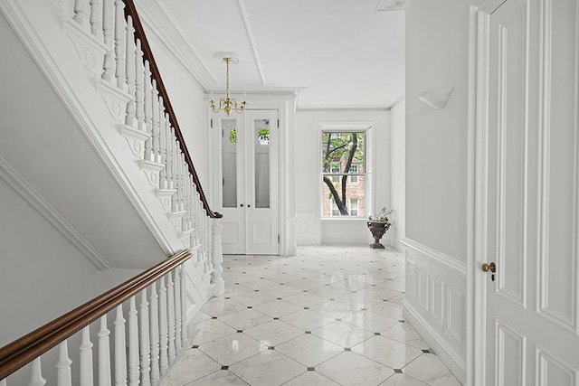 entrance foyer with wainscoting, stairway, a notable chandelier, ornamental molding, and a decorative wall
