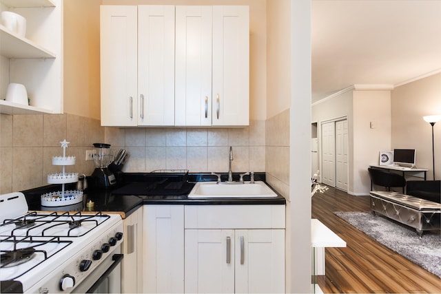 kitchen featuring white gas stove, a sink, backsplash, wood finished floors, and white cabinetry