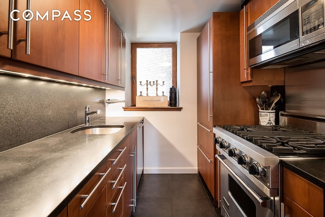 kitchen featuring baseboards, appliances with stainless steel finishes, a sink, and brown cabinets