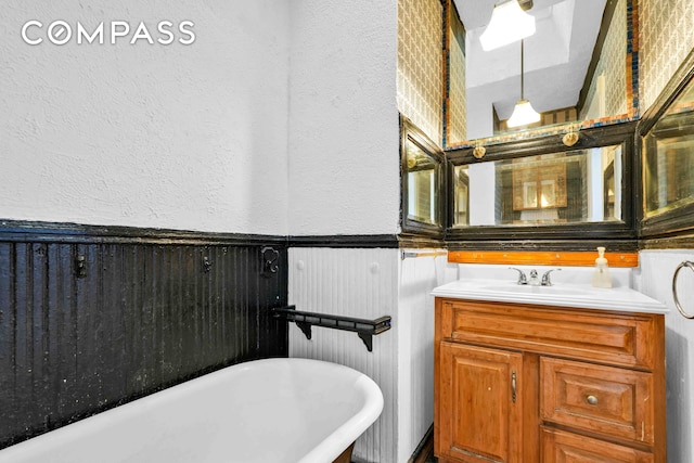 full bathroom with vanity, a soaking tub, a textured wall, and a wainscoted wall