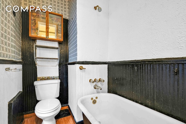 full bathroom featuring a freestanding bath, a textured wall, wainscoting, and toilet