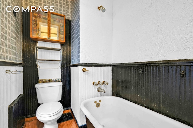 full bathroom with toilet, a soaking tub, wood finished floors, and wallpapered walls