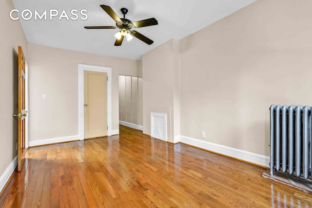 interior space featuring a ceiling fan, radiator heating unit, hardwood / wood-style flooring, and baseboards