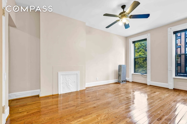 empty room featuring ceiling fan, radiator heating unit, baseboards, and wood-type flooring