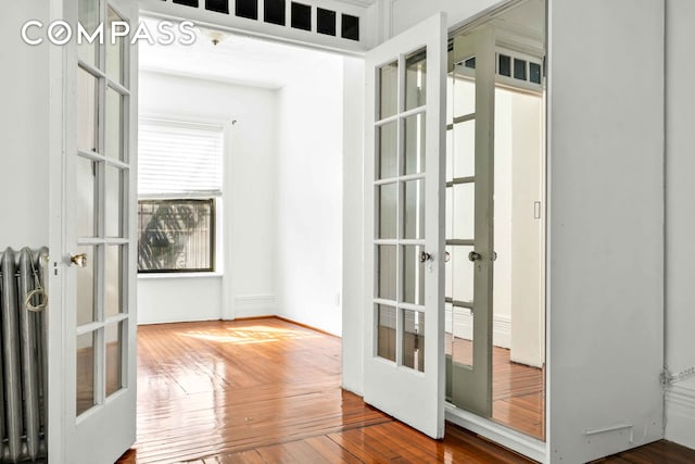 hall with hardwood / wood-style floors, radiator heating unit, and french doors