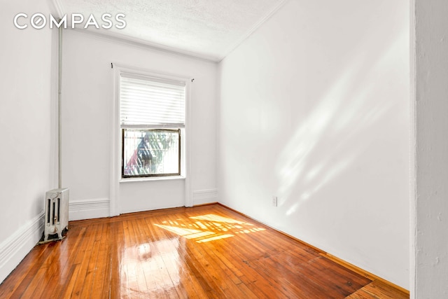 spare room with a textured ceiling, crown molding, hardwood / wood-style flooring, and radiator