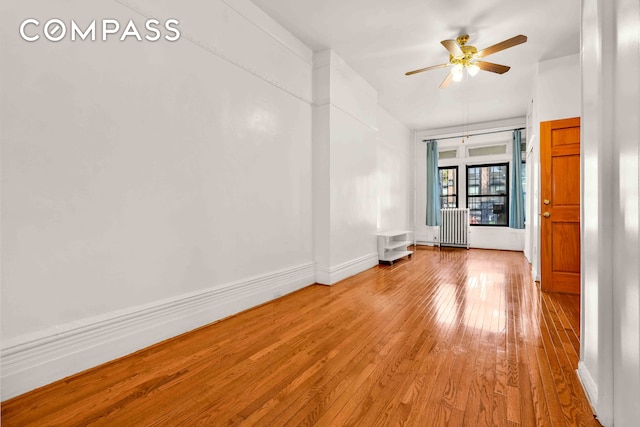 unfurnished room featuring a ceiling fan, radiator heating unit, light wood-style floors, and baseboards