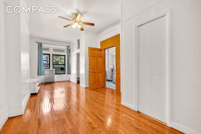 unfurnished bedroom with a ceiling fan, light wood-type flooring, baseboards, and radiator heating unit