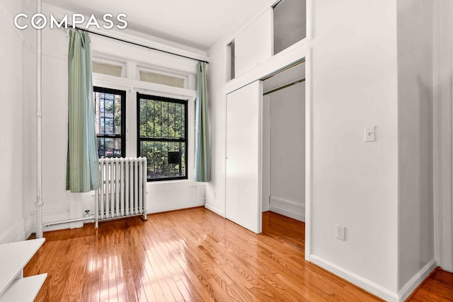 unfurnished bedroom featuring hardwood / wood-style flooring, radiator, and baseboards