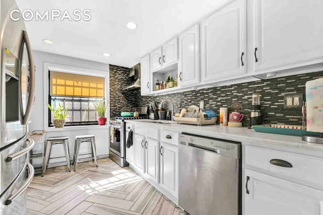 kitchen featuring appliances with stainless steel finishes, white cabinetry, a sink, and wall chimney range hood