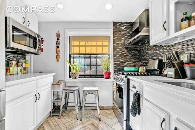 interior space featuring tasteful backsplash, stainless steel appliances, wall chimney range hood, white cabinetry, and recessed lighting