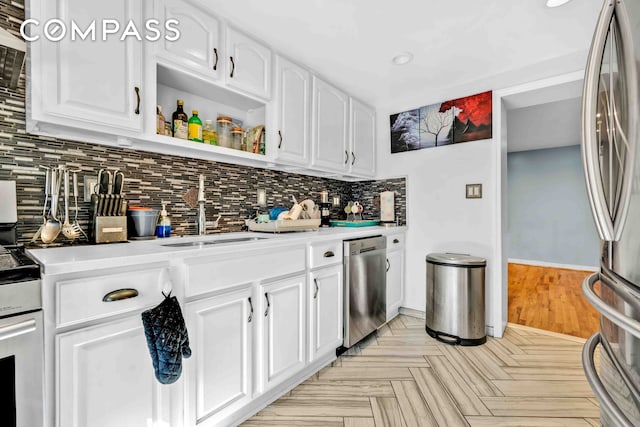 kitchen featuring backsplash, light countertops, white cabinets, stainless steel appliances, and a sink