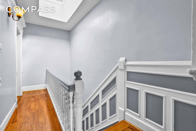 interior space featuring hardwood / wood-style floors, a skylight, an upstairs landing, and baseboards