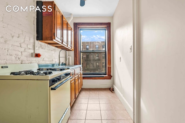 kitchen featuring light tile patterned floors, baseboards, brown cabinetry, white gas stove, and a sink