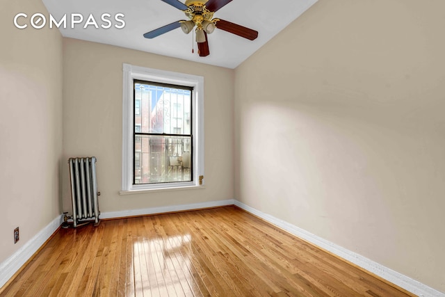 spare room with baseboards, ceiling fan, radiator heating unit, and light wood finished floors