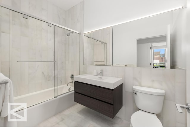 bathroom with tile walls, toilet, vanity, and shower / bath combination with glass door