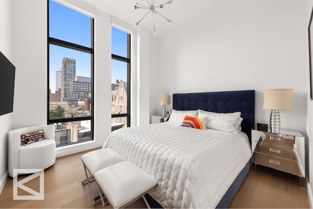 bedroom with a high ceiling, a notable chandelier, a city view, and wood finished floors