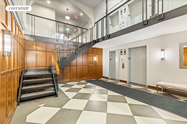 interior space featuring tile patterned floors, elevator, wood walls, and a towering ceiling