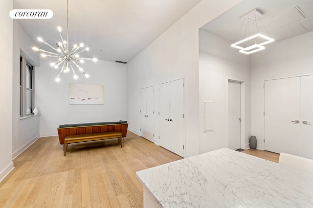 bedroom with two closets, a chandelier, light wood-style flooring, and baseboards