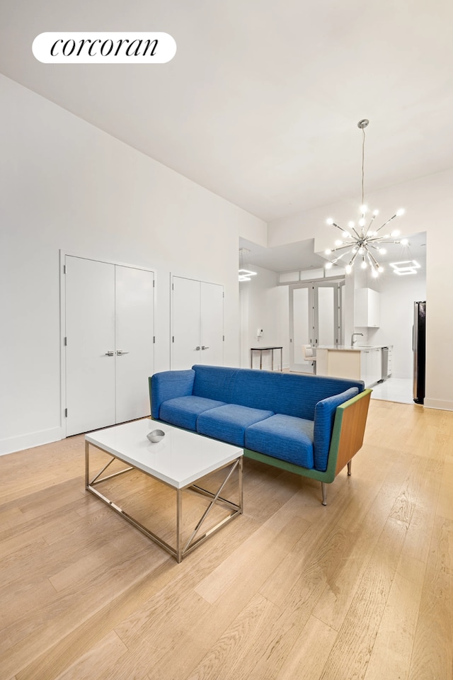 living room with light wood-type flooring, a chandelier, and baseboards