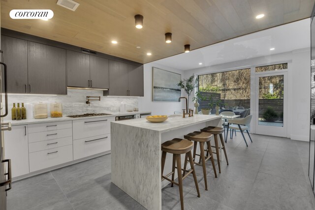 kitchen with tasteful backsplash, visible vents, stainless steel gas stovetop, modern cabinets, and a kitchen island with sink