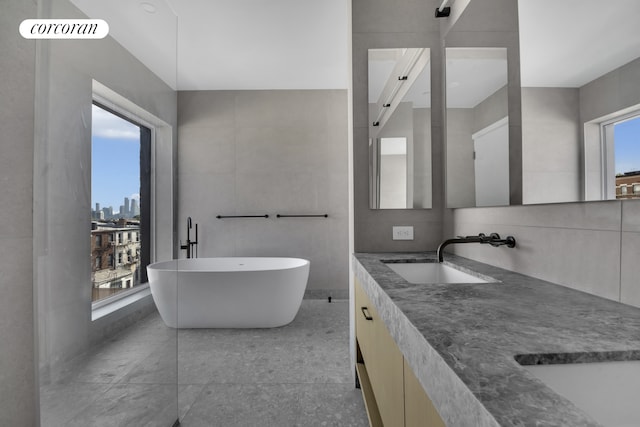 bathroom with tile walls, double vanity, a soaking tub, a view of city, and a sink