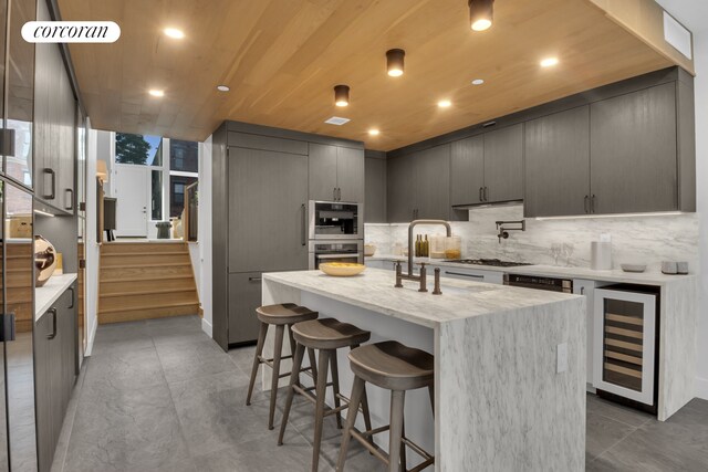 kitchen featuring a breakfast bar, an island with sink, a sink, decorative backsplash, and wine cooler