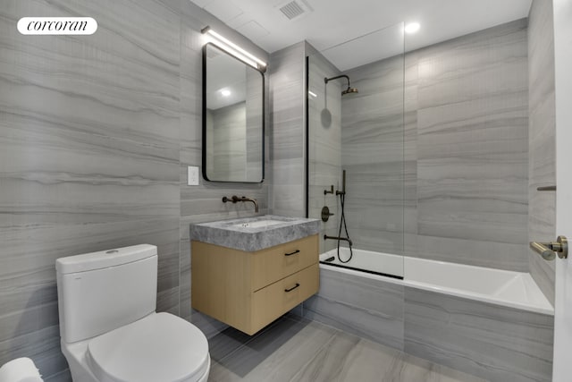 full bathroom with tiled shower / bath, vanity, toilet, and tile walls