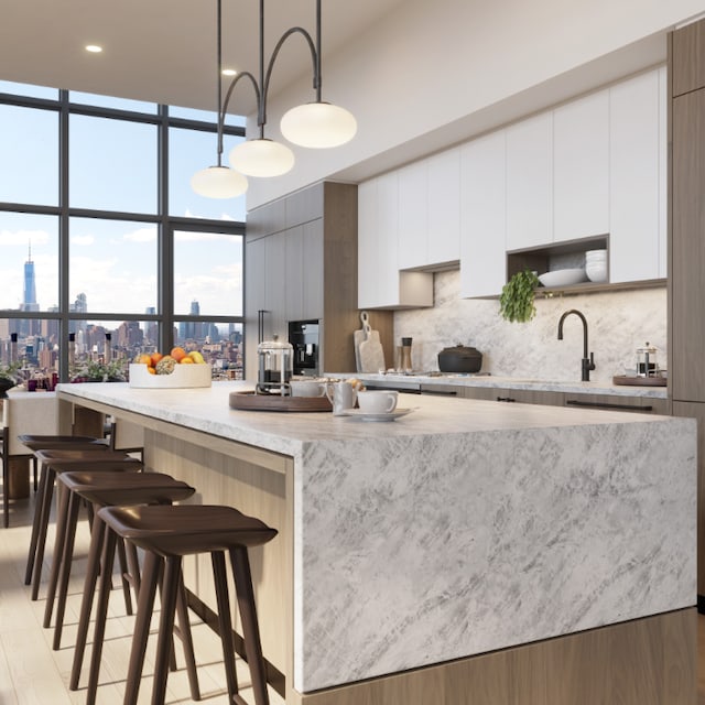 kitchen featuring white cabinetry, a kitchen breakfast bar, an island with sink, and hanging light fixtures