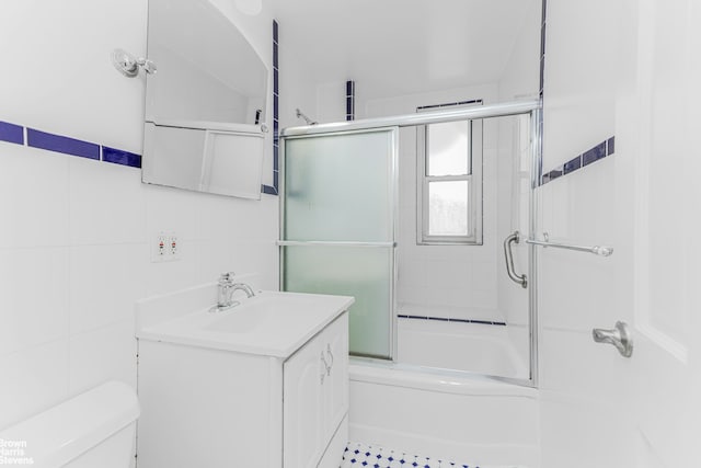 full bath featuring toilet, combined bath / shower with glass door, tile walls, and vanity