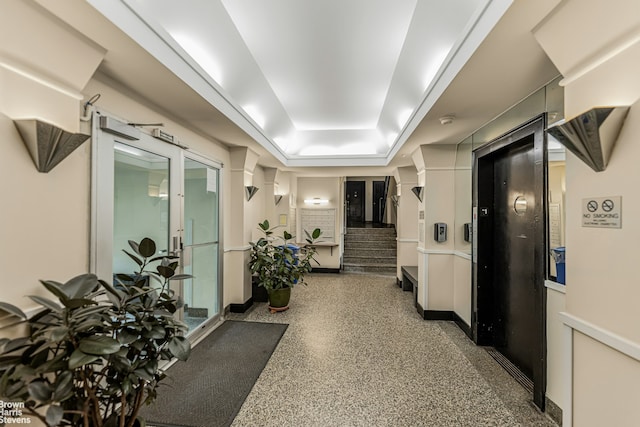 hallway with stairs, speckled floor, a raised ceiling, and elevator