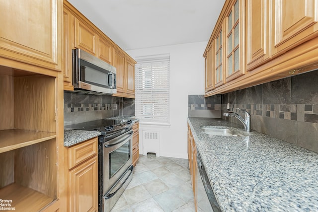 kitchen with light stone countertops, a sink, appliances with stainless steel finishes, radiator, and glass insert cabinets