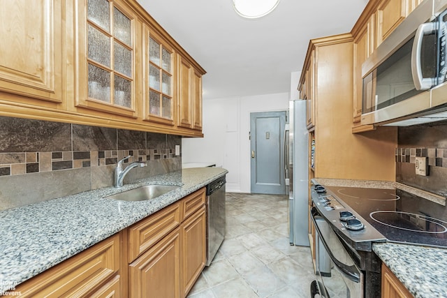 kitchen featuring tasteful backsplash, appliances with stainless steel finishes, glass insert cabinets, a sink, and light stone countertops