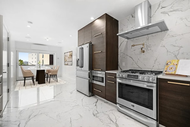 kitchen with wall chimney range hood, stainless steel appliances, tasteful backsplash, a wall unit AC, and dark brown cabinets