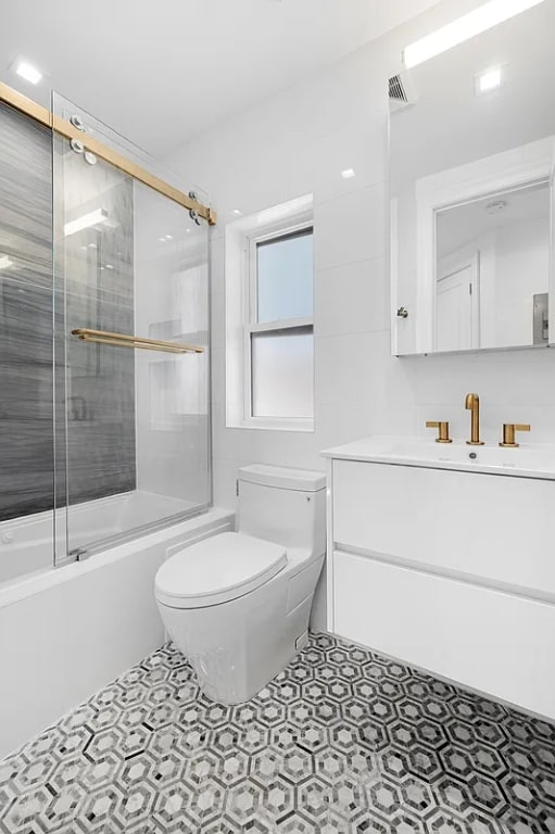 full bathroom featuring toilet, bath / shower combo with glass door, tile patterned flooring, and vanity