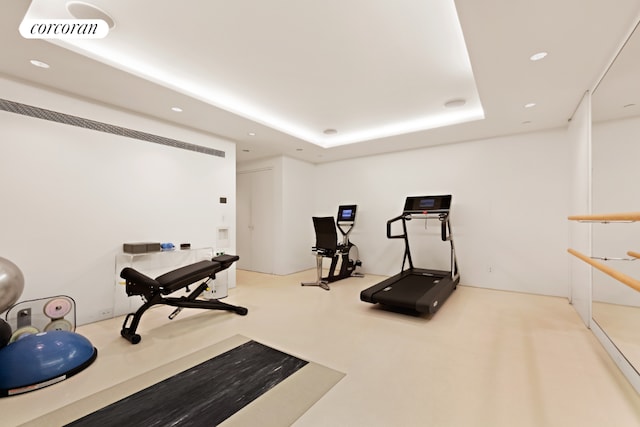 exercise room featuring a tray ceiling and light colored carpet