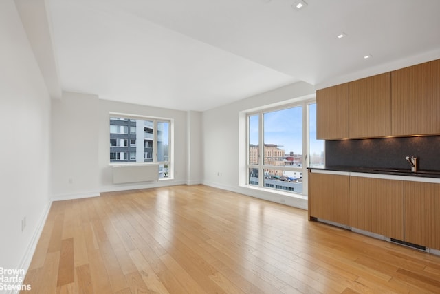 unfurnished living room with baseboards, light wood-style floors, and a sink