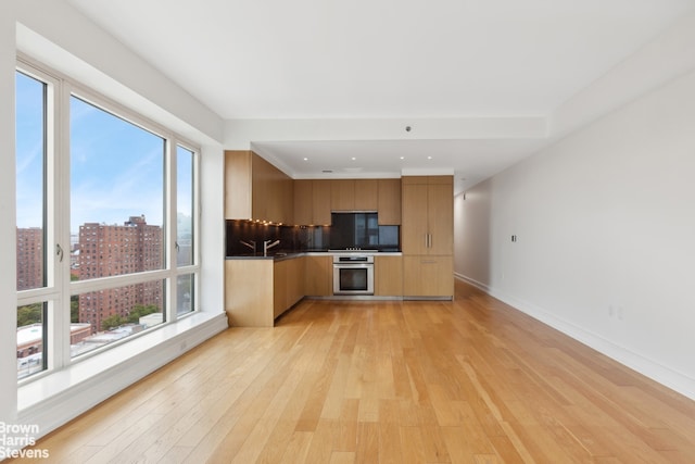 kitchen with baseboards, oven, light wood-style floors, modern cabinets, and tasteful backsplash