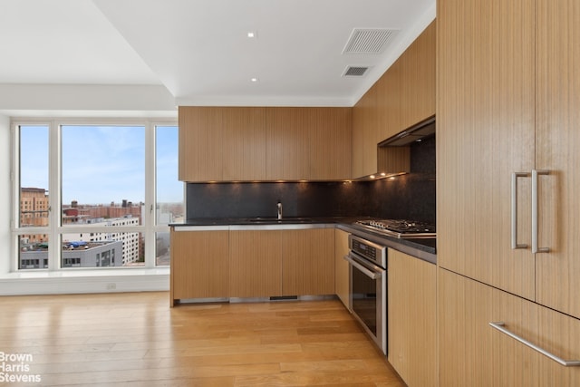 kitchen with dark countertops, visible vents, light wood-style flooring, stainless steel appliances, and a sink