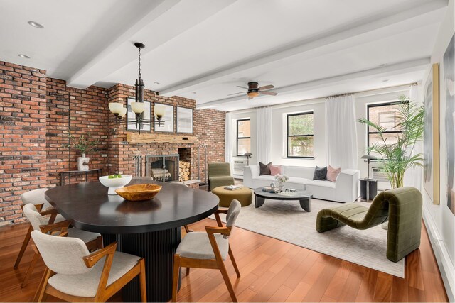 dining room with a brick fireplace, brick wall, beam ceiling, and light wood-type flooring