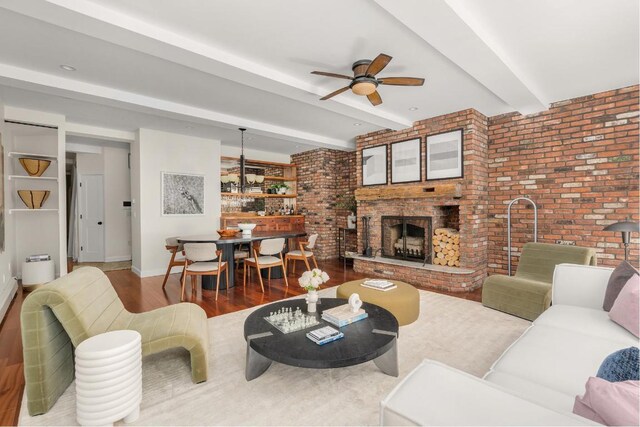 living room with light wood-type flooring, a brick fireplace, ceiling fan, and beamed ceiling