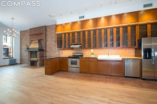 kitchen with sink, radiator, light hardwood / wood-style flooring, stainless steel appliances, and decorative light fixtures