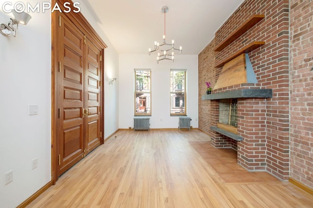 foyer with an inviting chandelier, a brick fireplace, radiator heating unit, and light wood-type flooring