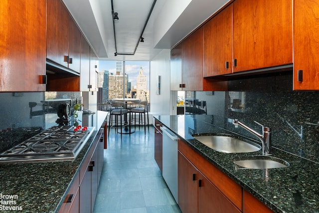 kitchen with track lighting, stainless steel appliances, dark stone countertops, decorative backsplash, and sink