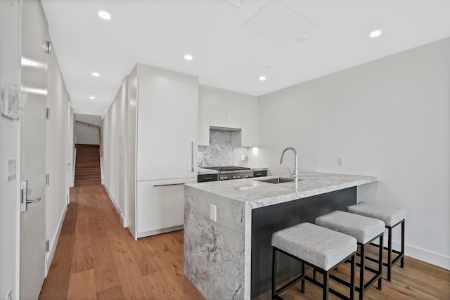 kitchen featuring a breakfast bar area, a peninsula, light wood-style flooring, a sink, and white cabinets